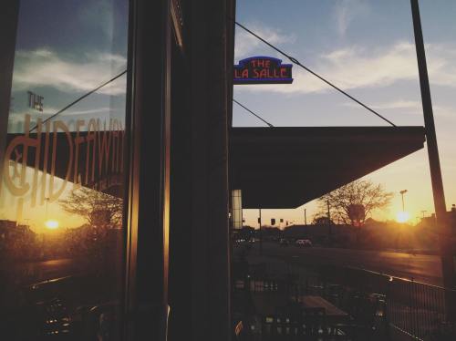 Sunset view reflecting on a window, with a neon sign reading "La Salle" and outdoor seating visible.