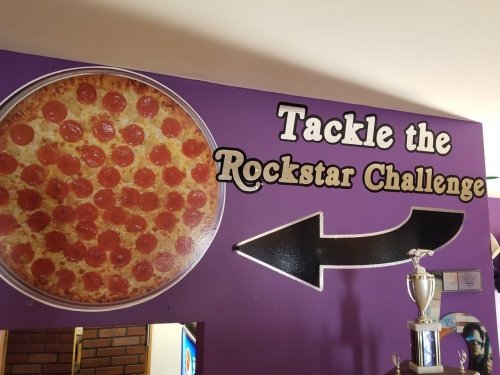 A wall sign featuring a large pizza graphic and text reading "Tackle the Rockstar Challenge" with an arrow pointing left.