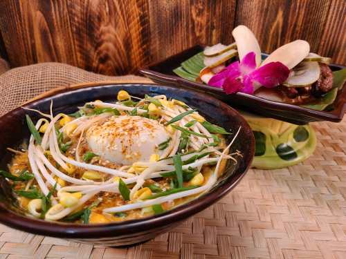 A bowl of noodles topped with a poached egg, bean sprouts, and green onions, alongside a plate of assorted dishes.