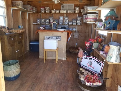 A cozy farm store interior with wooden walls, shelves of containers, and a display of local products and decorations.