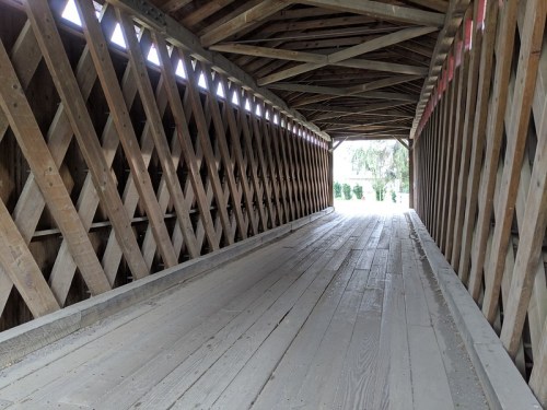 Interior view of a covered wooden bridge, featuring a wooden floor and crisscrossed wooden supports.