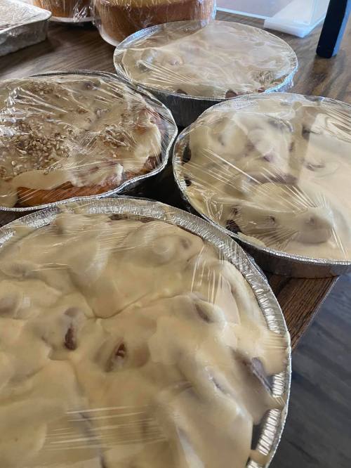 Four covered pies in aluminum pans, topped with creamy frosting, sitting on a wooden table.