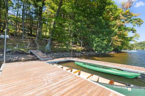 A wooden dock with a green kayak, surrounded by trees and calm water on a sunny day.