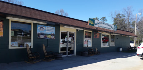A small deli with a green exterior, rocking chairs on the porch, and a sign reading "Hogshooter Deli."