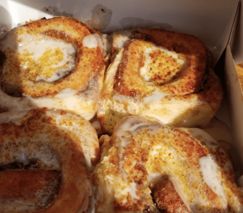 Four freshly baked cinnamon rolls with creamy icing, arranged in a box, golden brown and gooey.