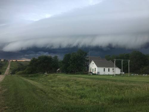 A white house sits near a road under a dramatic, low-hanging cloud formation in a stormy sky.