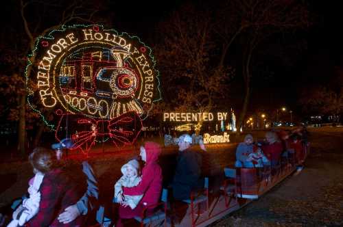 A festive train display with colorful lights, featuring families enjoying a holiday ride in a park at night.