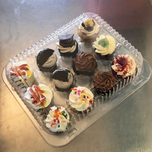 A clear container filled with assorted colorful cupcakes, featuring various toppings and flavors.