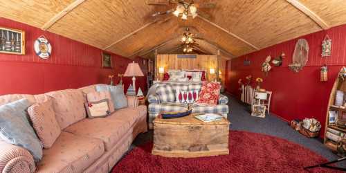 Cozy interior of a rustic room with red walls, wooden ceiling, a sofa, and decorative nautical elements.