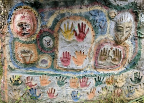 Colorful handprints and faces are painted on a textured wall, showcasing various artistic designs and patterns.