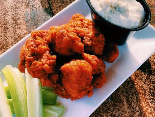 Plate of crispy buffalo cauliflower bites with celery sticks and a side of ranch dressing.