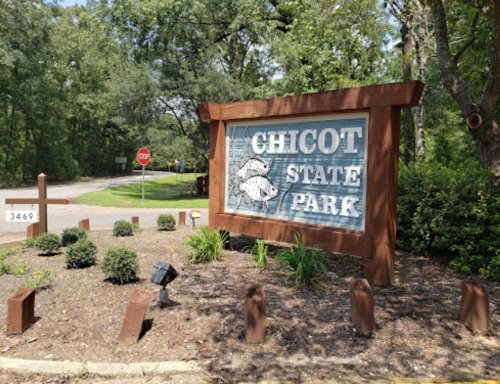Sign for Chicot State Park surrounded by greenery, with a stop sign visible in the background.