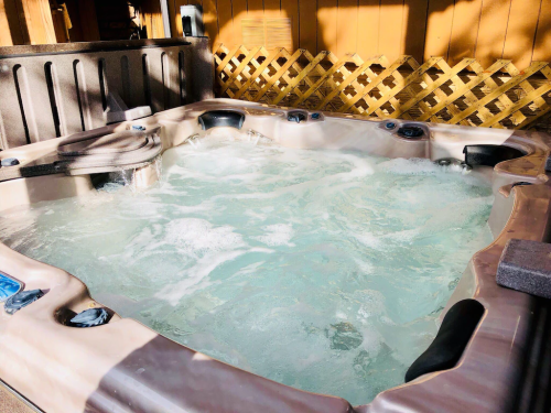 A hot tub filled with bubbling water, surrounded by wooden fencing and sunlight.