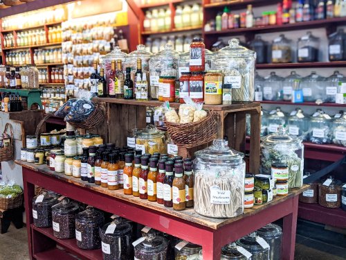 A vibrant display of jars and bottles filled with various spices, sauces, and ingredients on a wooden table in a market.
