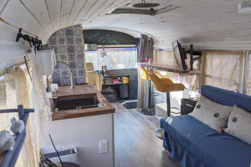 Interior of a converted bus featuring a cozy living area, kitchen, and workspace with natural light and wooden accents.