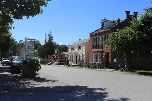 A quiet street scene featuring charming buildings, trees, and pedestrians on a sunny day.