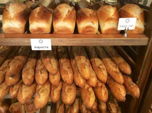 A display of freshly baked baguettes and French loaves on wooden shelves, labeled for identification.