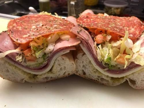A close-up of a sandwich filled with layers of meats, lettuce, tomatoes, and spices on a sliced hoagie roll.