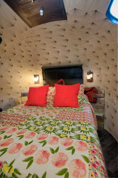 Cozy bedroom with a patterned quilt, two red pillows, and textured walls, featuring soft lighting and a window.