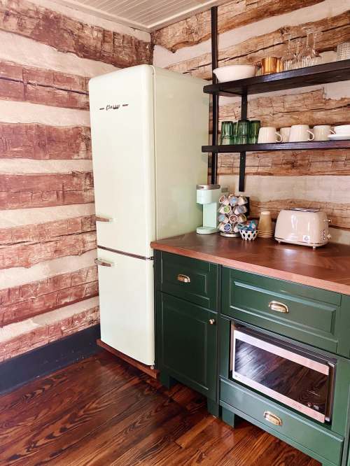 A vintage green fridge stands next to a wooden wall, with a countertop featuring a toaster and various kitchenware.