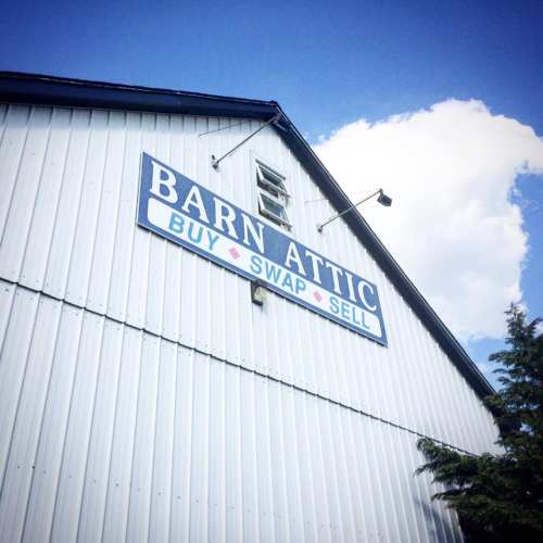 A blue barn with a sign reading "Barn Attic - Buy, Swap, Sell" against a clear sky.