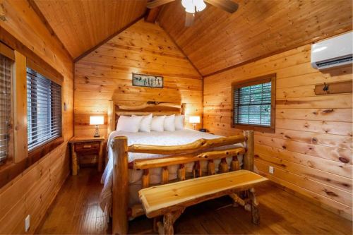 Cozy wooden cabin interior featuring a queen bed, bedside tables, and a rustic bench. Warm, inviting atmosphere.
