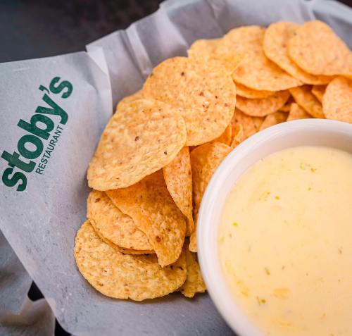 A bowl of creamy cheese dip next to a pile of crispy tortilla chips on a paper-lined plate.