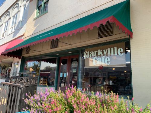 Exterior of Starkville Cafe with a green awning and colorful flowers in front, showcasing a charming street scene.