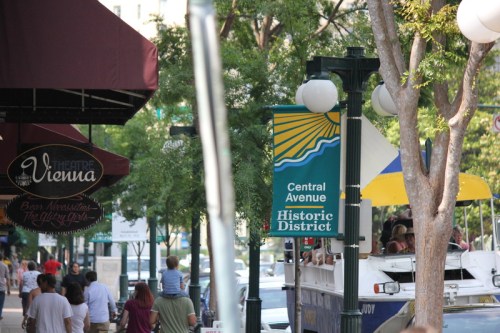 A bustling street scene featuring signs for Theatre Vienna and Central Avenue Historic District, with people walking by.