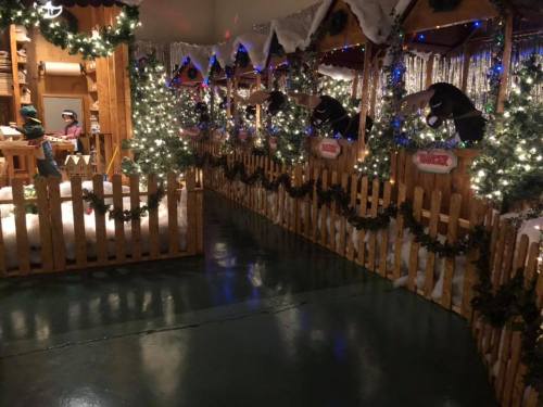 A festive indoor scene with wooden stalls, holiday lights, and decorations, creating a cozy, winter atmosphere.
