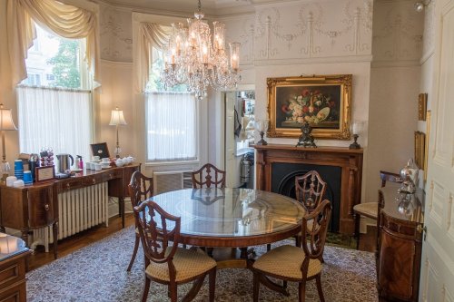 Elegant dining room featuring a round table, chandelier, and decorative artwork, with soft natural light filtering in.