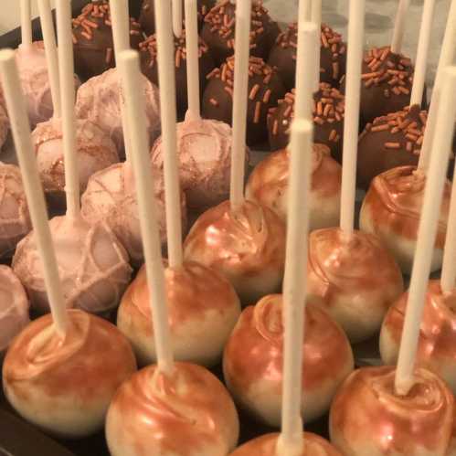 A tray of assorted cake pops, featuring chocolate, white, and caramel coatings, topped with sprinkles.