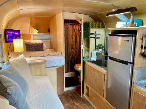 Cozy interior of a camper van featuring a bed, kitchenette, bathroom, and living area with modern decor.