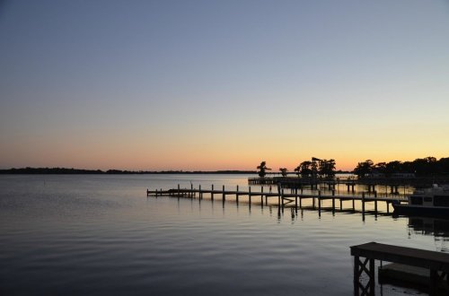 A serene lake at sunset, with calm waters reflecting the colorful sky and a wooden pier extending into the water.