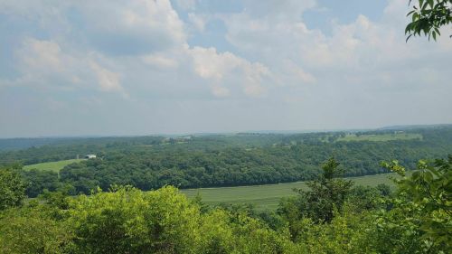 A panoramic view of lush green hills and fields under a partly cloudy sky.