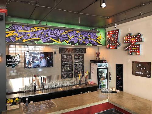 A vibrant bar with graffiti art, a chalkboard menu, and a variety of drinks displayed in a modern setting.