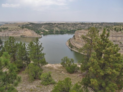 A serene landscape featuring a river winding through rocky cliffs, surrounded by green trees under a cloudy sky.