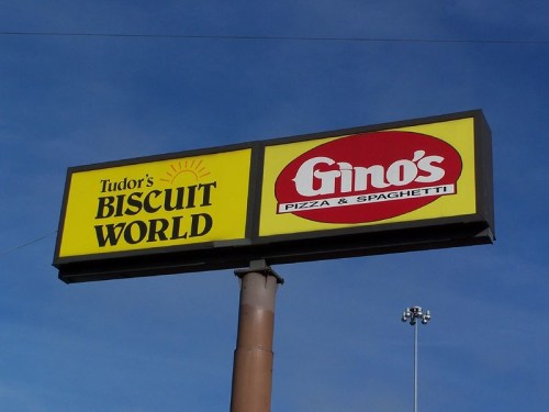 Sign for Tudor's Biscuit World and Gino's Pizza & Spaghetti against a blue sky.