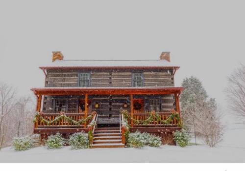 A charming log cabin covered in snow, adorned with festive greenery on the porch, surrounded by a winter landscape.