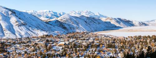 A snowy mountain landscape with a small town nestled in the valley, surrounded by towering peaks and clear blue skies.