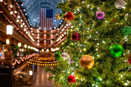 A decorated Christmas tree with colorful ornaments and lights, set in a festive indoor space with an American flag.