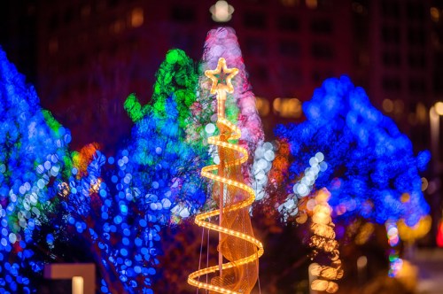 A brightly lit Christmas tree with a star on top, surrounded by colorful, blurred holiday lights.