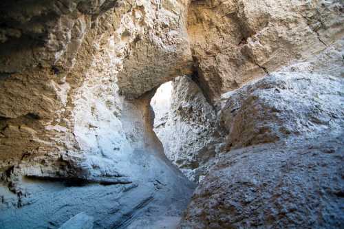 A narrow canyon with rocky walls and a natural archway, illuminated by sunlight filtering through the opening.