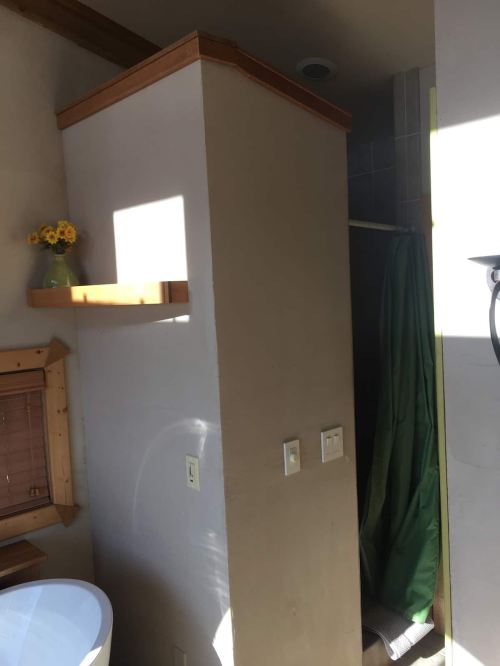 A bathroom corner featuring a shower with a green curtain, a shelf, and a vase of flowers on a ledge.