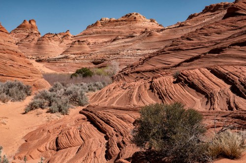 A stunning desert landscape featuring layered red rock formations and sparse vegetation under a clear blue sky.