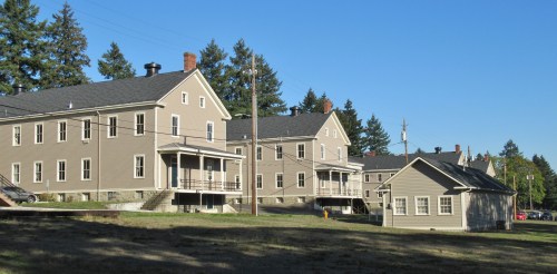 A row of historic, two-story houses with porches, surrounded by trees and a clear blue sky.