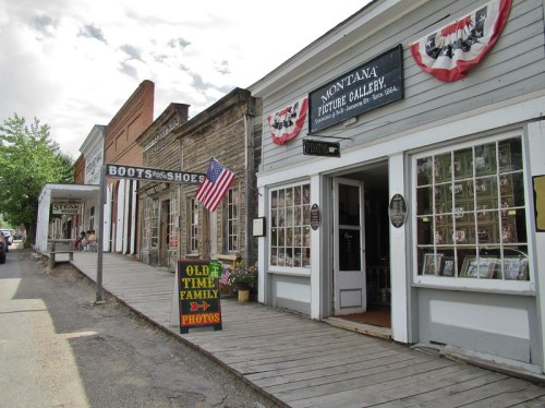 Historic street view featuring shops with wooden sidewalks, an American flag, and a sign for family photos.