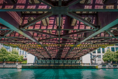 View from underneath a bridge, showcasing intricate metal beams and reflections on the water below.