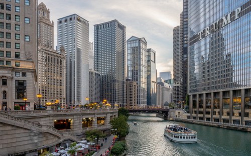 A scenic view of Chicago's skyline along the river, featuring modern skyscrapers and a boat on the water.