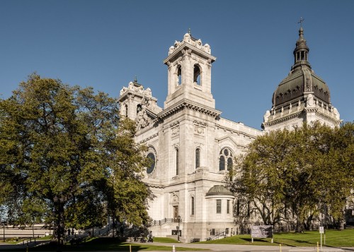 Historic stone building with ornate architecture, surrounded by trees under a clear blue sky.